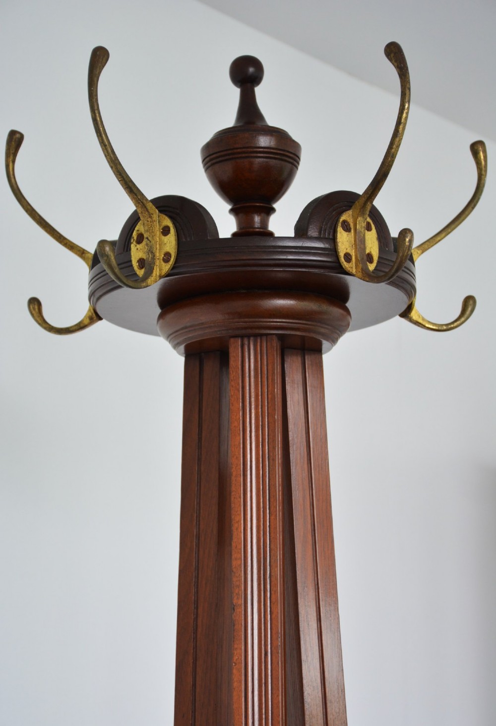 A tall freestanding dark walnut coat stand featuring a slatted central column, brass hooks, a turned finial, and four splayed feet. View X