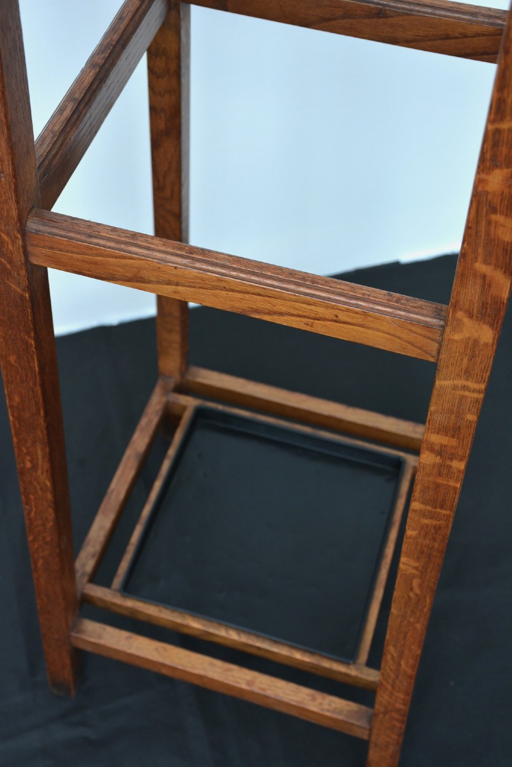 A tall solid oak freestanding coat stand featuring a tapered frame, four upper brass hooks, and a black metal drip tray at the base. View III