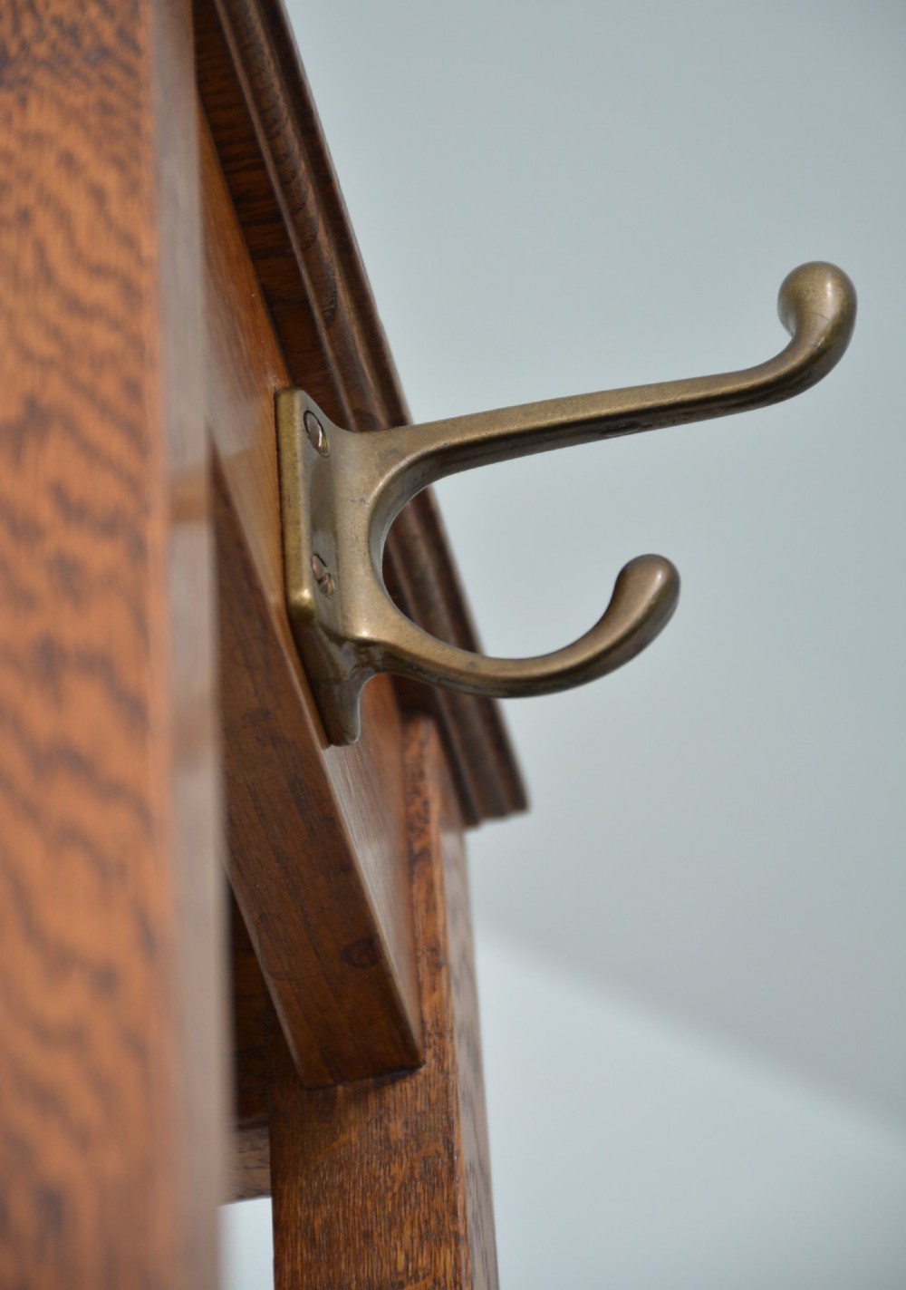 A tall solid oak freestanding coat stand featuring a tapered frame, four upper brass hooks, and a black metal drip tray at the base. View XV