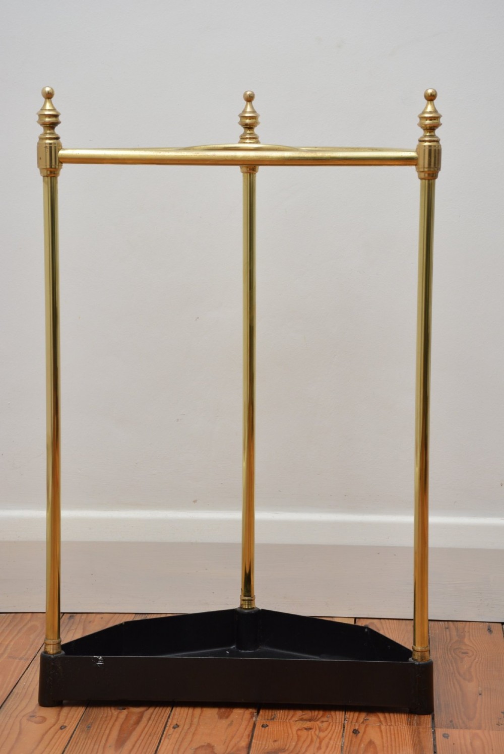 A brass demi-lune umbrella stand featuring three vertical posts topped with turned finials, internal division bars, and a black metal drip tray base. View IV