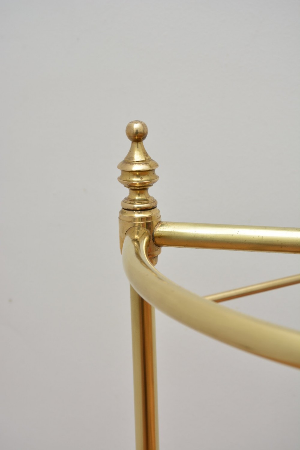A brass demi-lune umbrella stand featuring three vertical posts topped with turned finials, internal division bars, and a black metal drip tray base. View V