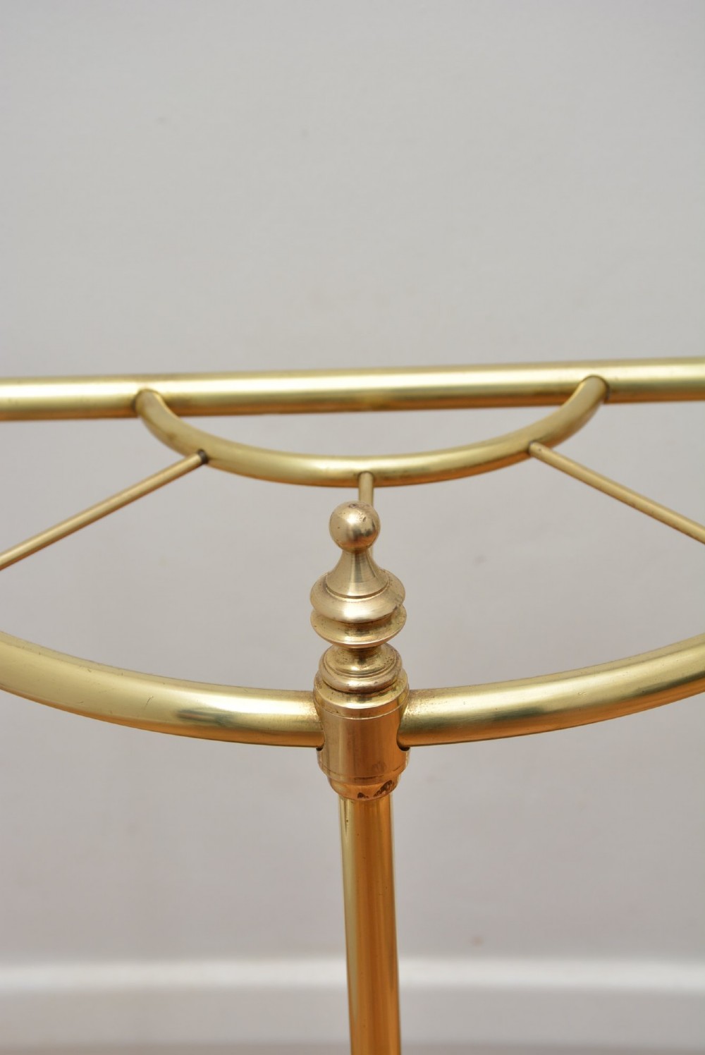 A brass demi-lune umbrella stand featuring three vertical posts topped with turned finials, internal division bars, and a black metal drip tray base. View VII