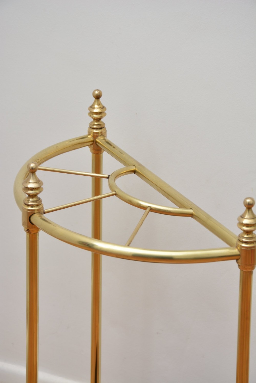 A brass demi-lune umbrella stand featuring three vertical posts topped with turned finials, internal division bars, and a black metal drip tray base. View VIII