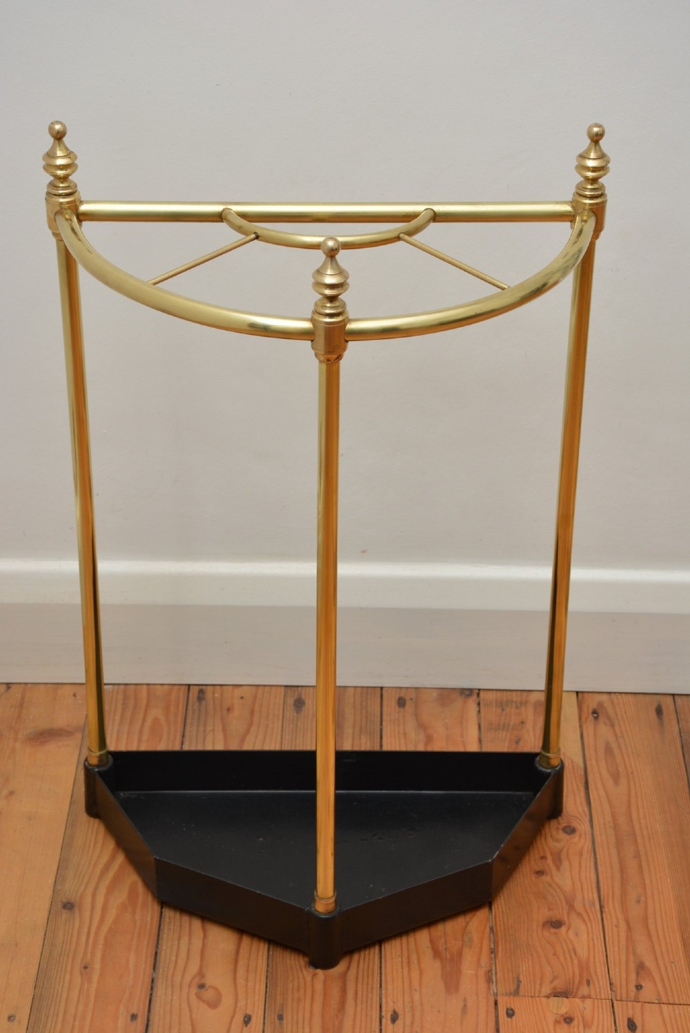 A brass demi-lune umbrella stand featuring three vertical posts topped with turned finials, internal division bars, and a black metal drip tray base.