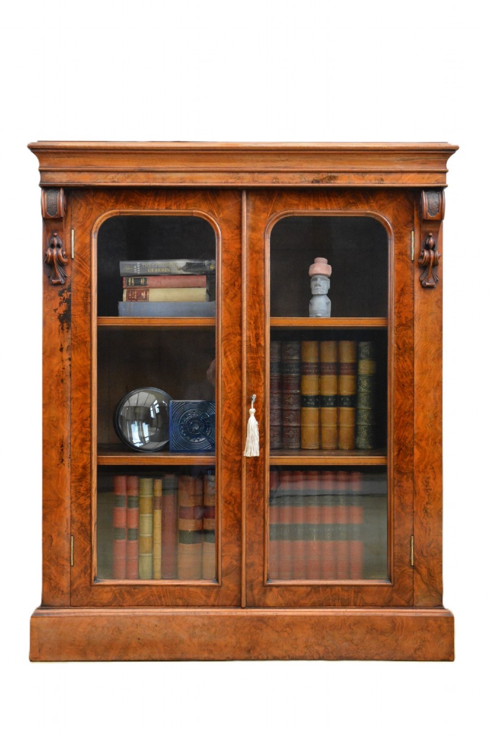 An English Victorian low bookcase made of figured walnut with two arched glass doors, carved corbels, and internal shelves.