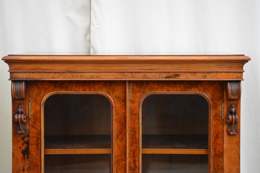 An English Victorian low bookcase made of figured walnut with two arched glass doors, carved corbels, and internal shelves. View IX