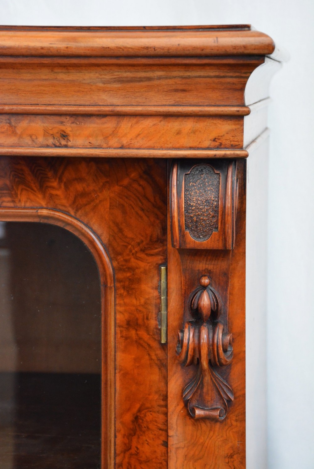 An English Victorian low bookcase made of figured walnut with two arched glass doors, carved corbels, and internal shelves. View X