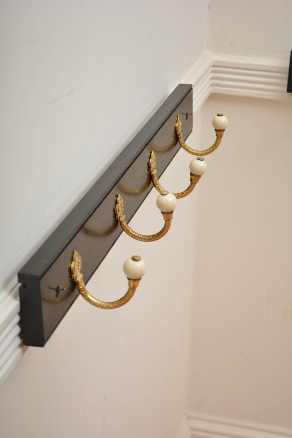 A wall-mounted black wooden coat rack featuring four decorative brass hooks with round white ceramic finials. View V
