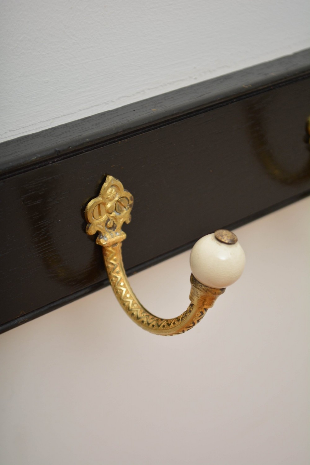 A wall-mounted black wooden coat rack featuring four decorative brass hooks with round white ceramic finials. View IX