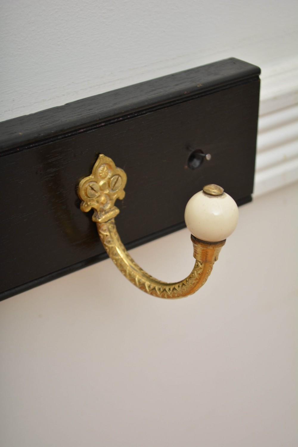 A wall-mounted black wooden coat rack featuring four decorative brass hooks with round white ceramic finials. View X