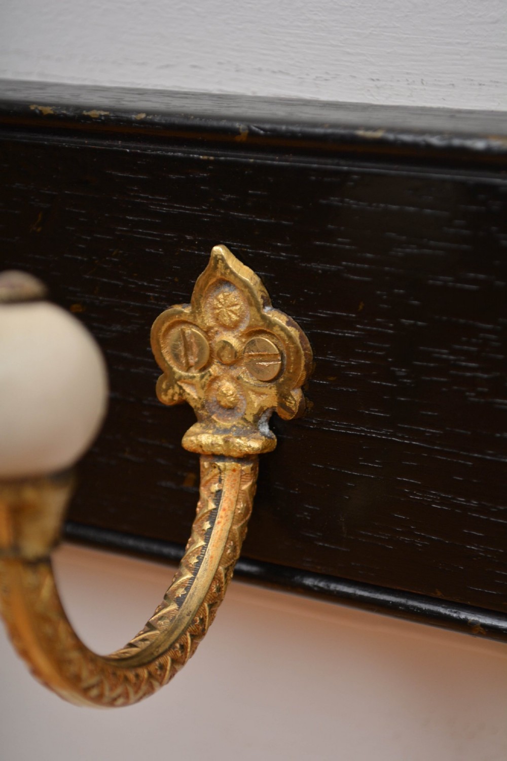 A wall-mounted black wooden coat rack featuring four decorative brass hooks with round white ceramic finials. View XI