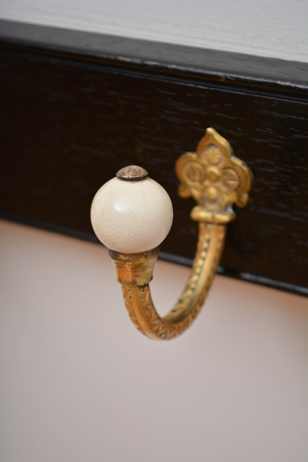 A wall-mounted black wooden coat rack featuring four decorative brass hooks with round white ceramic finials. View XII