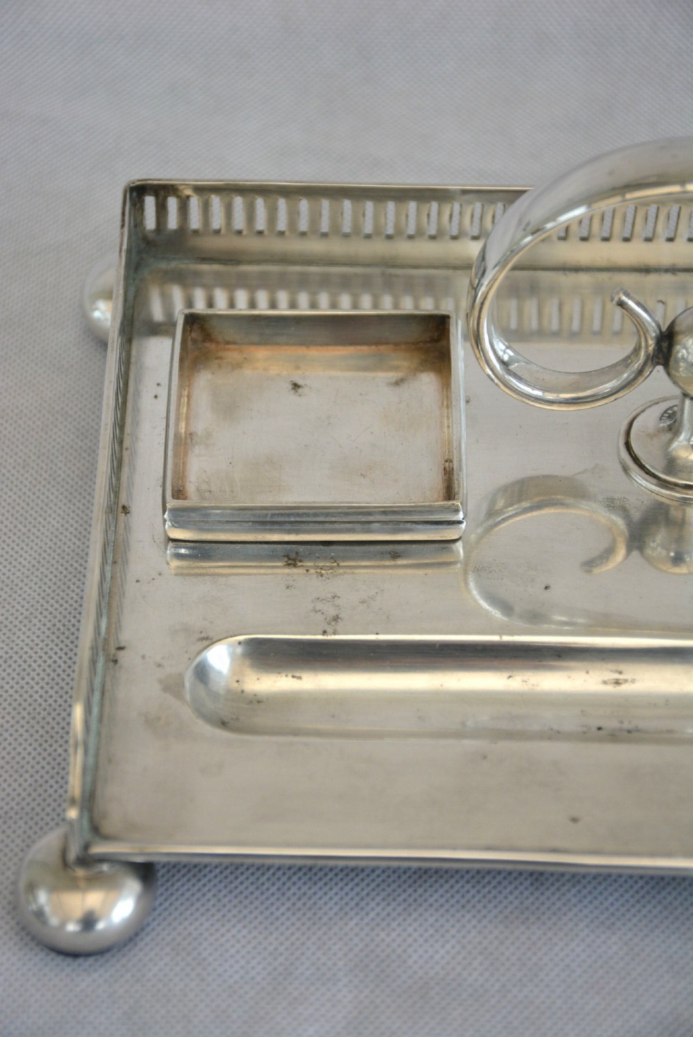 A rectangular silver-plated inkstand featuring a pierced gallery, central handle, built-in pen groove, and two clear glass inkwells with silver lids resting on ball feet. View X