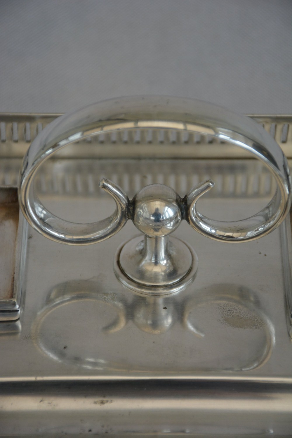 A rectangular silver-plated inkstand featuring a pierced gallery, central handle, built-in pen groove, and two clear glass inkwells with silver lids resting on ball feet. View XII