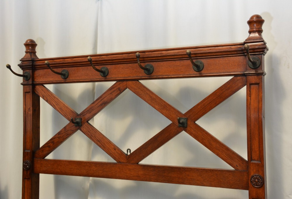 A tall Victorian Gothic oak hall stand featuring cross-braced lattice framing, metal coat pegs, finial tops, and carved architectural supports. View V
