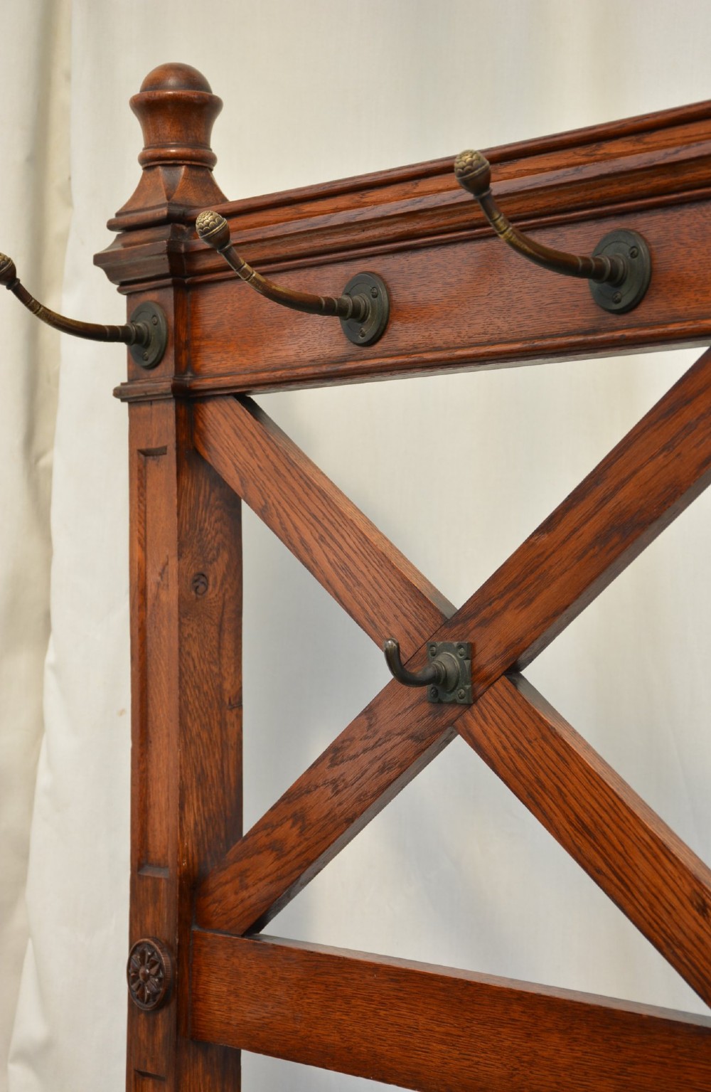 A tall Victorian Gothic oak hall stand featuring cross-braced lattice framing, metal coat pegs, finial tops, and carved architectural supports. View VI