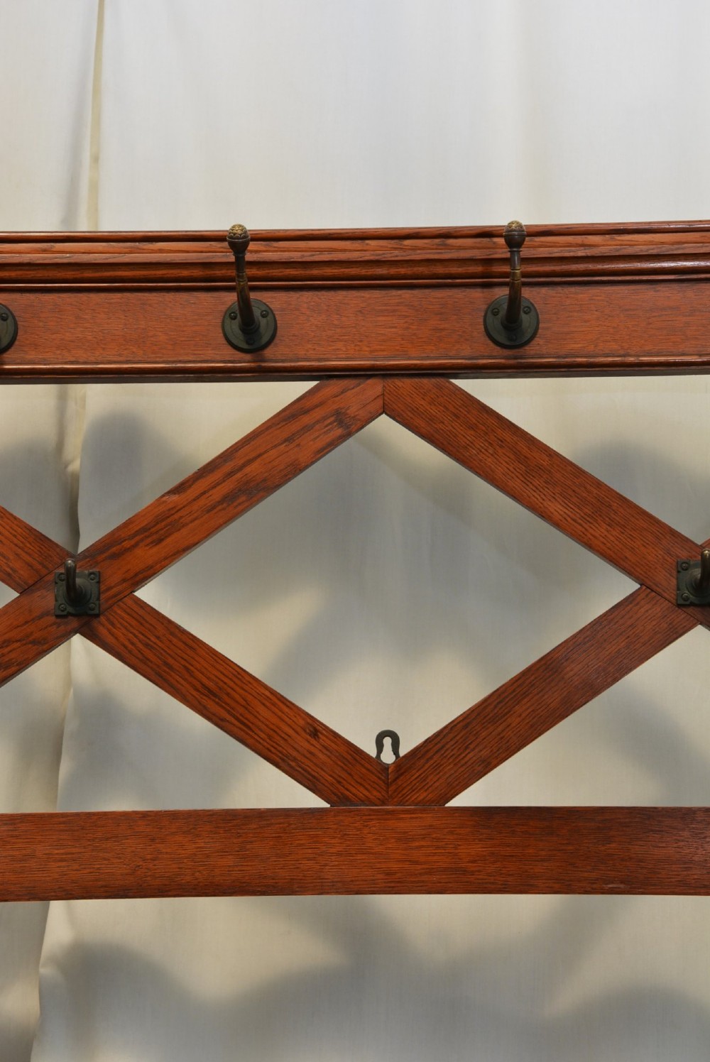 A tall Victorian Gothic oak hall stand featuring cross-braced lattice framing, metal coat pegs, finial tops, and carved architectural supports. View VIII