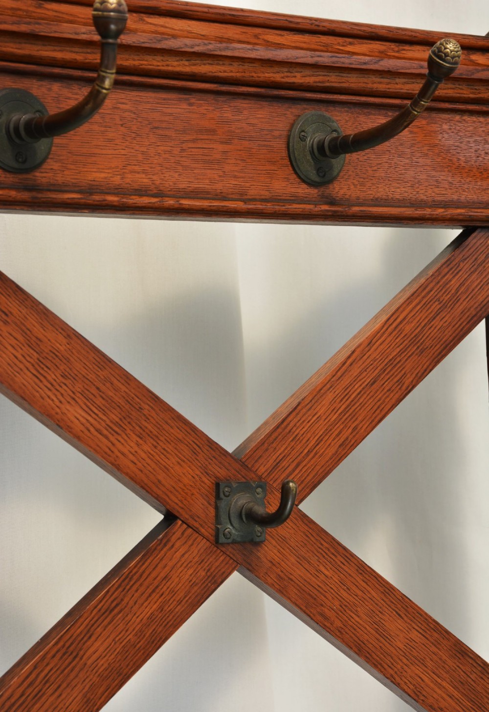 A tall Victorian Gothic oak hall stand featuring cross-braced lattice framing, metal coat pegs, finial tops, and carved architectural supports. View X