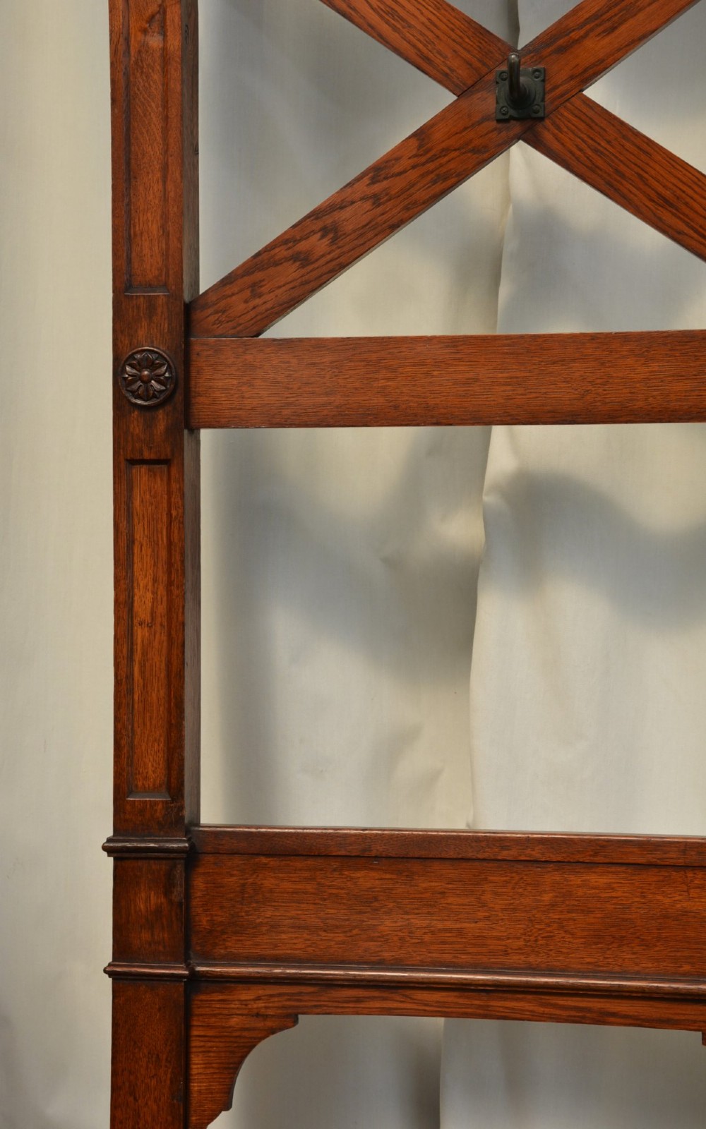 A tall Victorian Gothic oak hall stand featuring cross-braced lattice framing, metal coat pegs, finial tops, and carved architectural supports. View XIV