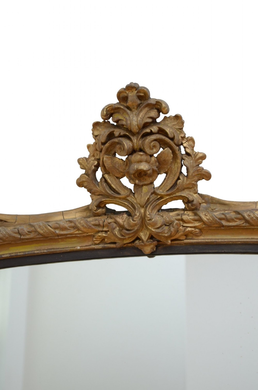 A tall arched overmantel mirror featuring a gold gilded frame decorated with an intricate carved top cresting and scroll base feet. View VI