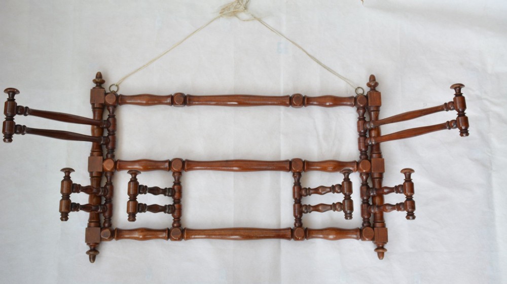 A wall-mounted dark wood coat rack constructed from turned spindles with multiple hanging pegs and decorative corner finials. View II