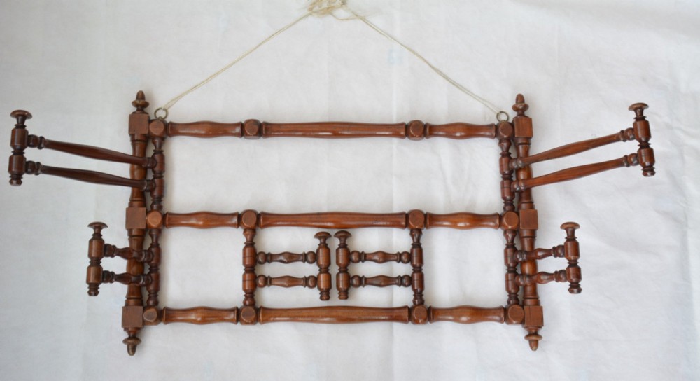 A wall-mounted dark wood coat rack constructed from turned spindles with multiple hanging pegs and decorative corner finials. View III