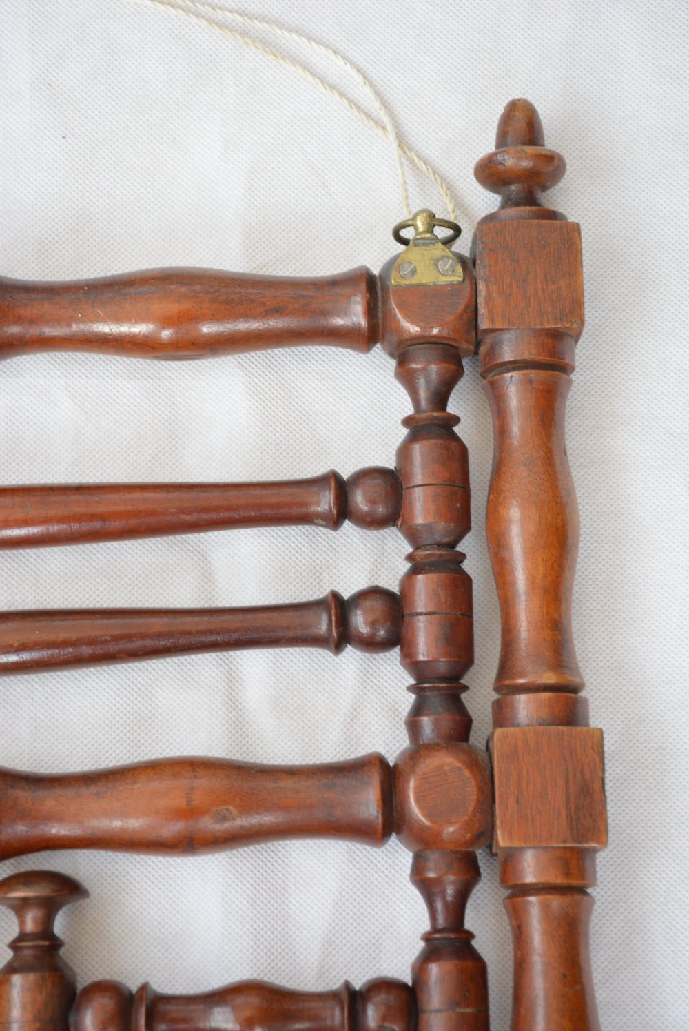 A wall-mounted dark wood coat rack constructed from turned spindles with multiple hanging pegs and decorative corner finials. View V