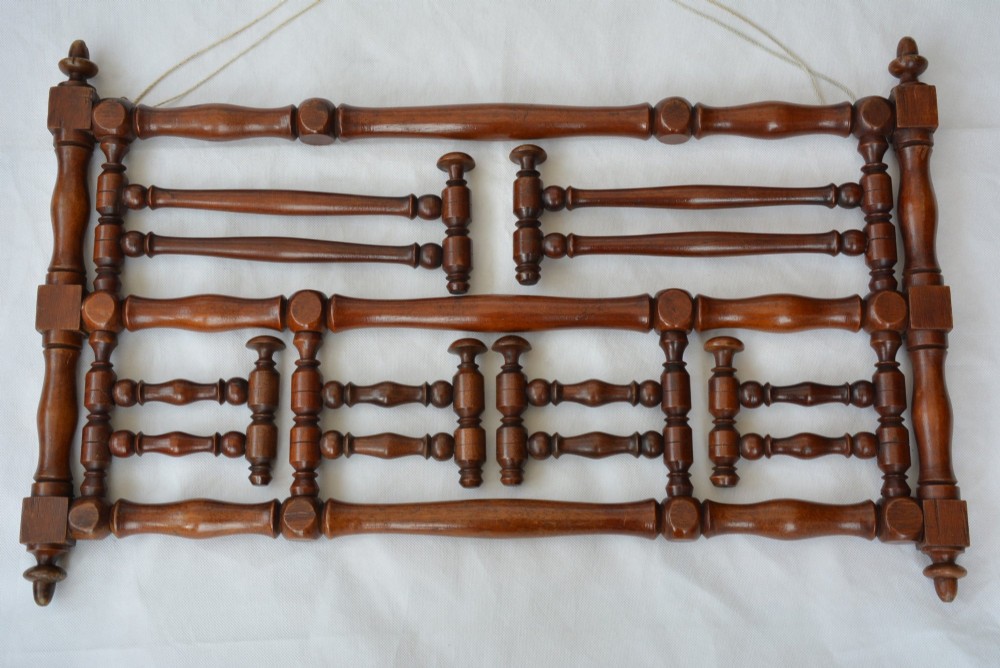 A wall-mounted dark wood coat rack constructed from turned spindles with multiple hanging pegs and decorative corner finials. View VI
