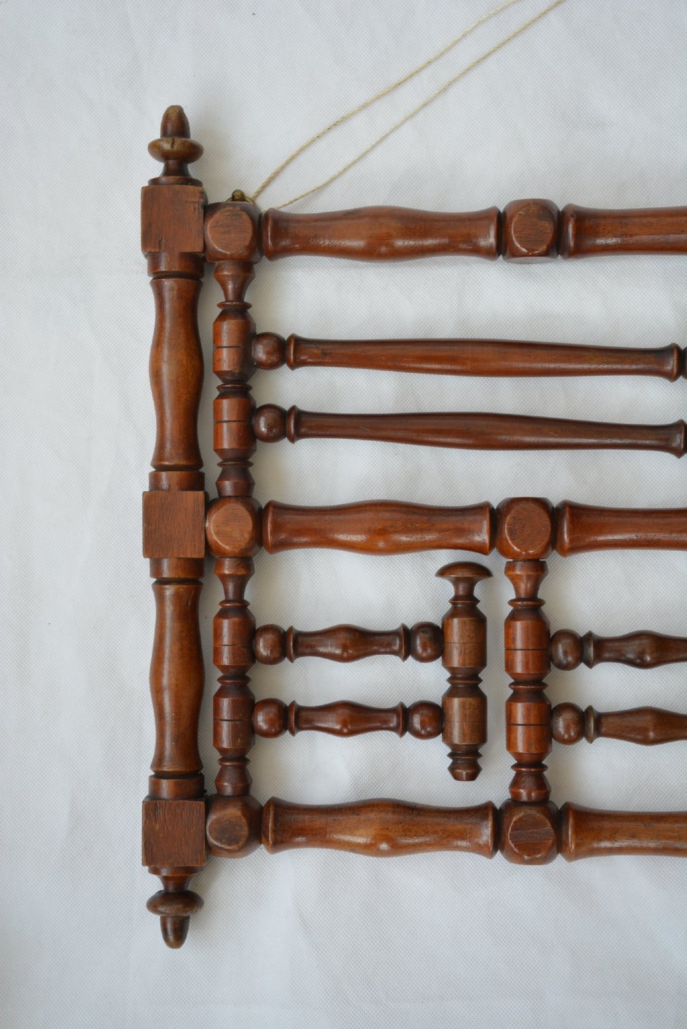 A wall-mounted dark wood coat rack constructed from turned spindles with multiple hanging pegs and decorative corner finials. View VII