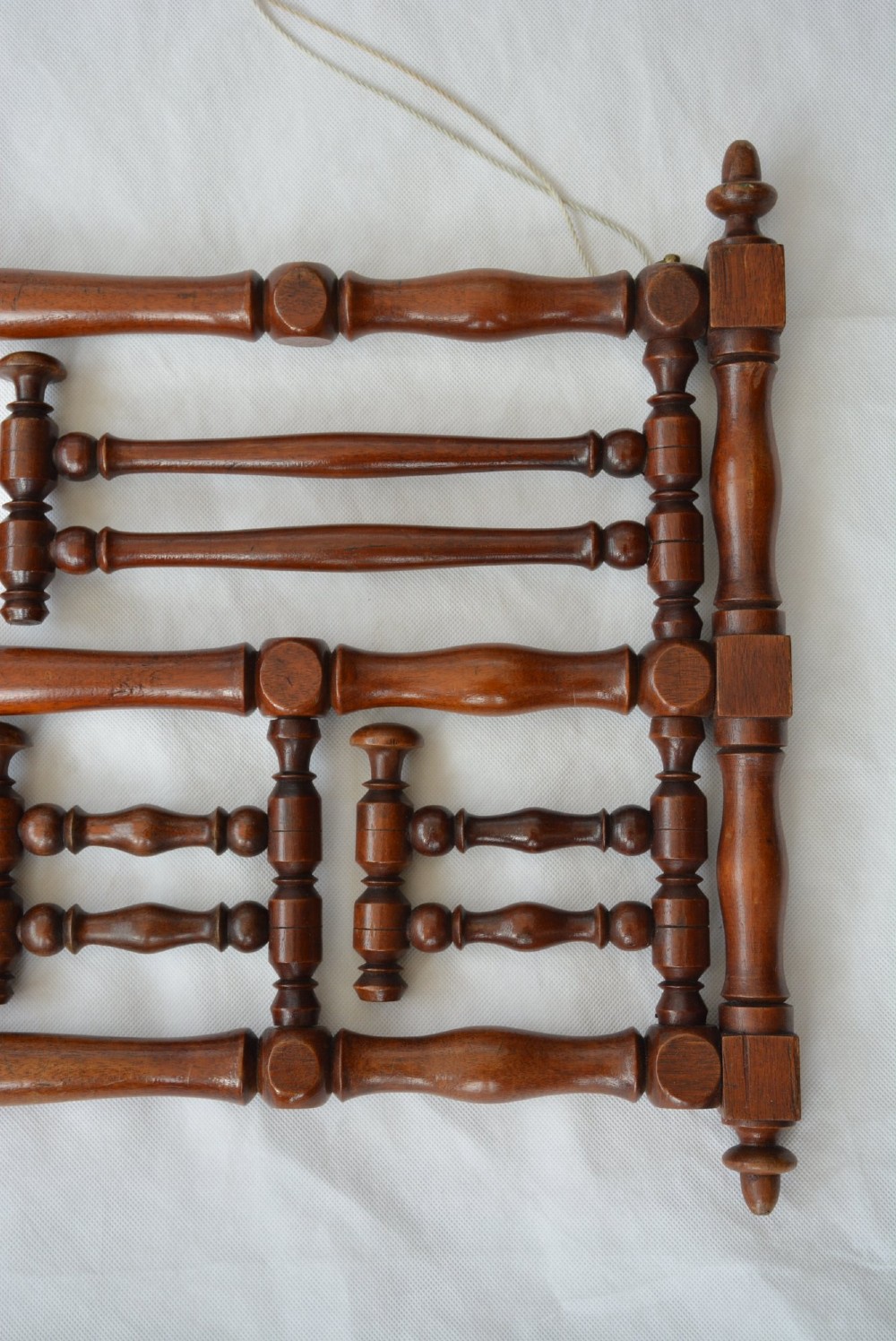 A wall-mounted dark wood coat rack constructed from turned spindles with multiple hanging pegs and decorative corner finials. View IX