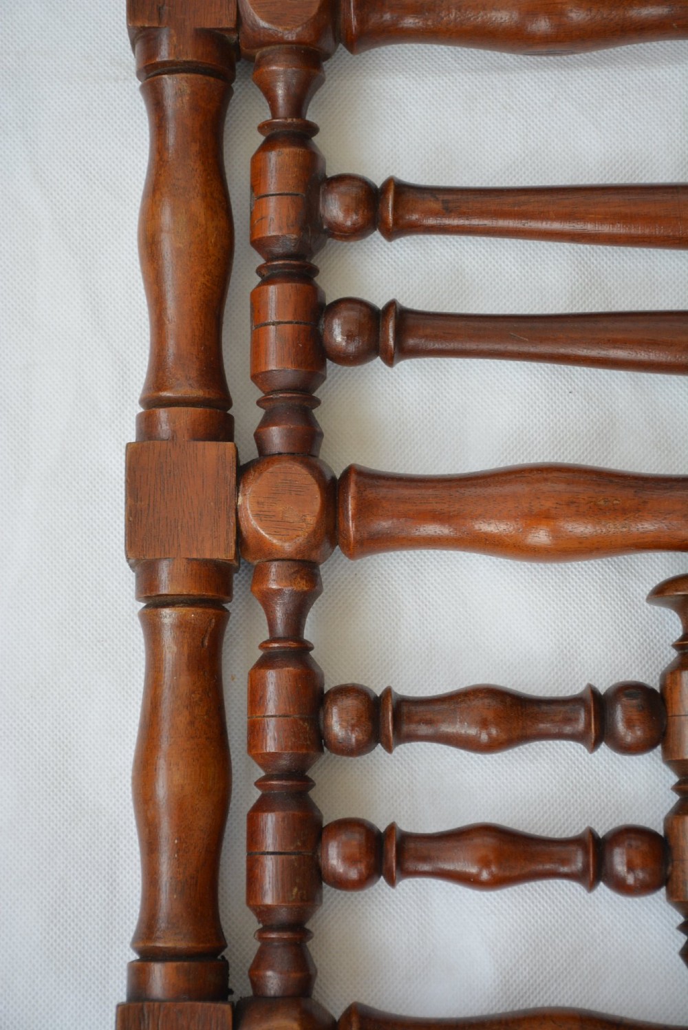 A wall-mounted dark wood coat rack constructed from turned spindles with multiple hanging pegs and decorative corner finials. View X