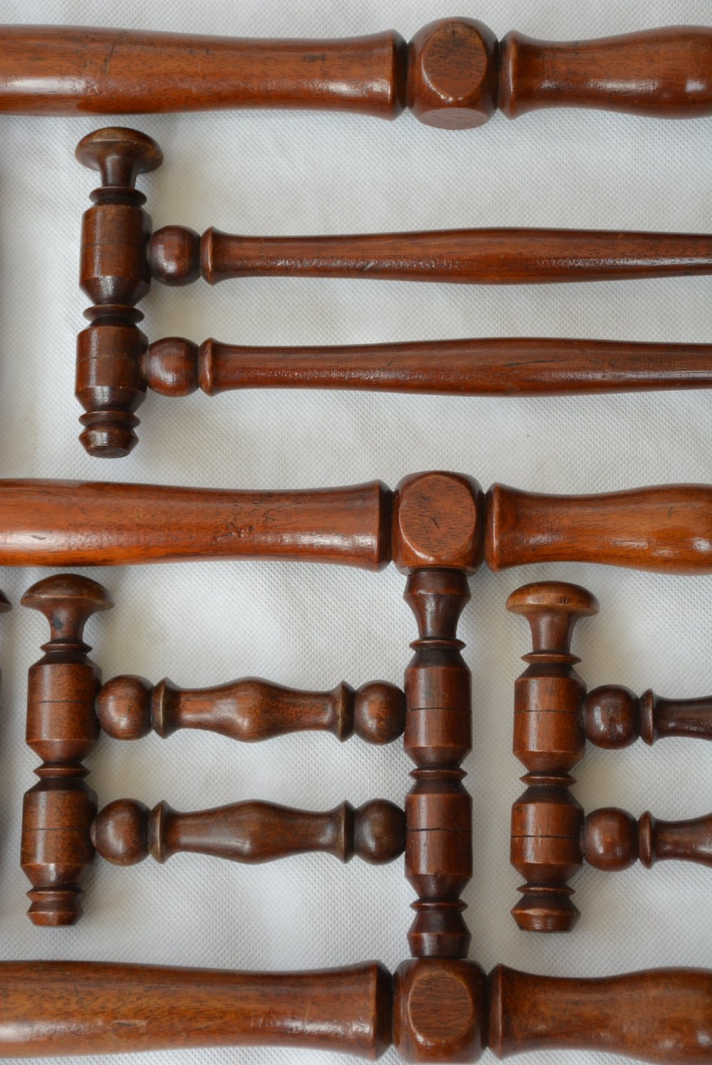 A wall-mounted dark wood coat rack constructed from turned spindles with multiple hanging pegs and decorative corner finials. View XII