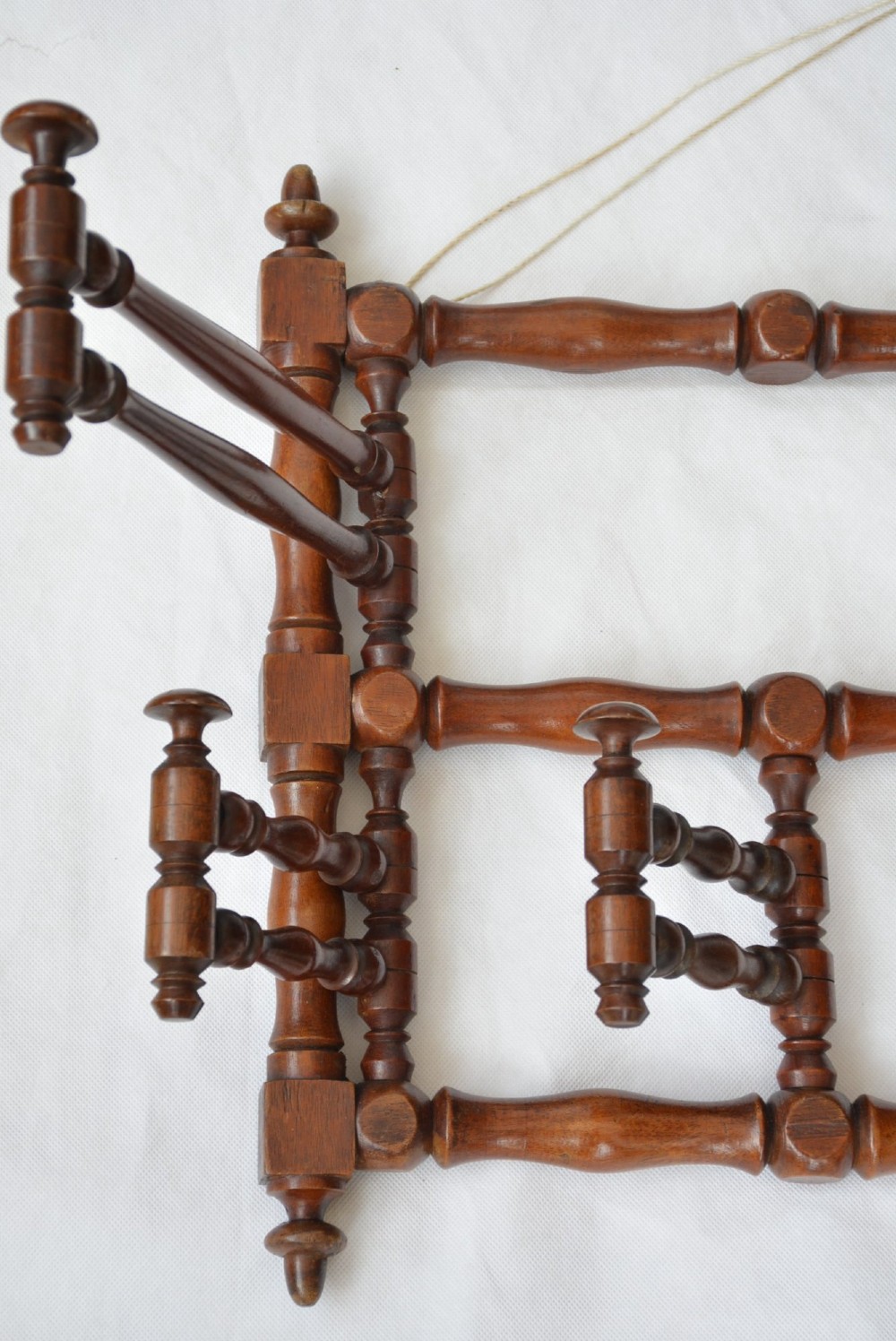 A wall-mounted dark wood coat rack constructed from turned spindles with multiple hanging pegs and decorative corner finials. View XIV