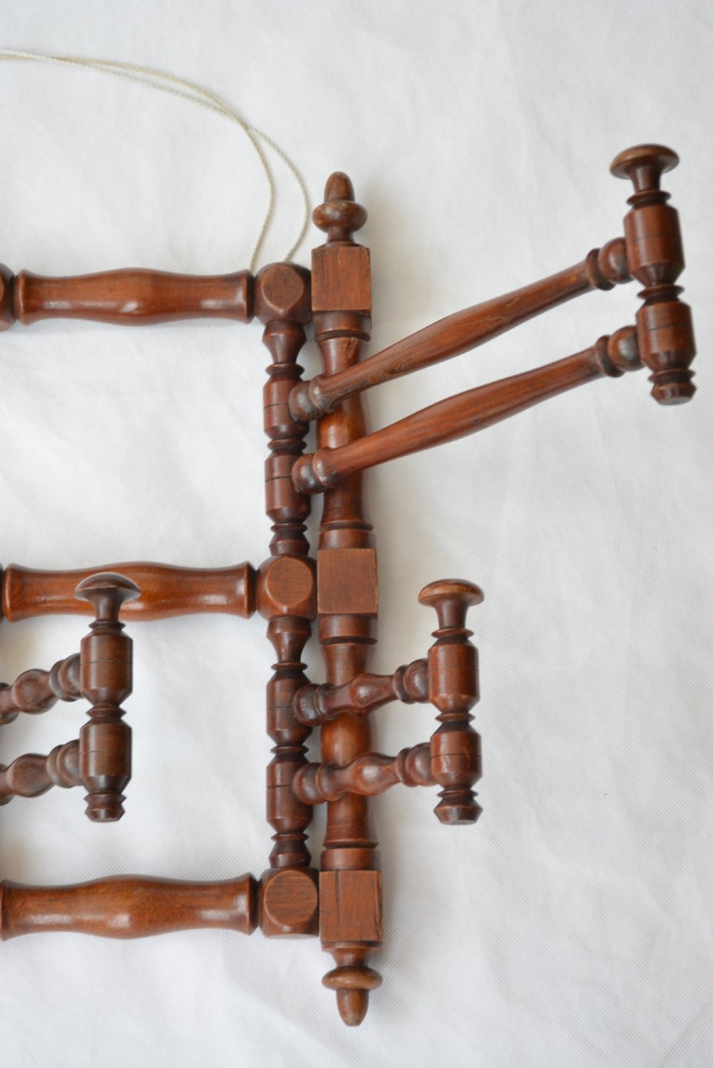 A wall-mounted dark wood coat rack constructed from turned spindles with multiple hanging pegs and decorative corner finials. View XV