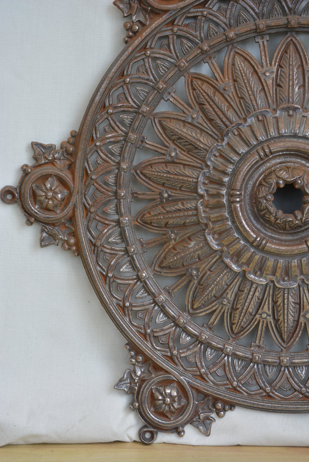 A circular Victorian cast iron ceiling rose featuring central feather relief detail surrounded by pierced openwork and ivy leaf border lugs. View V