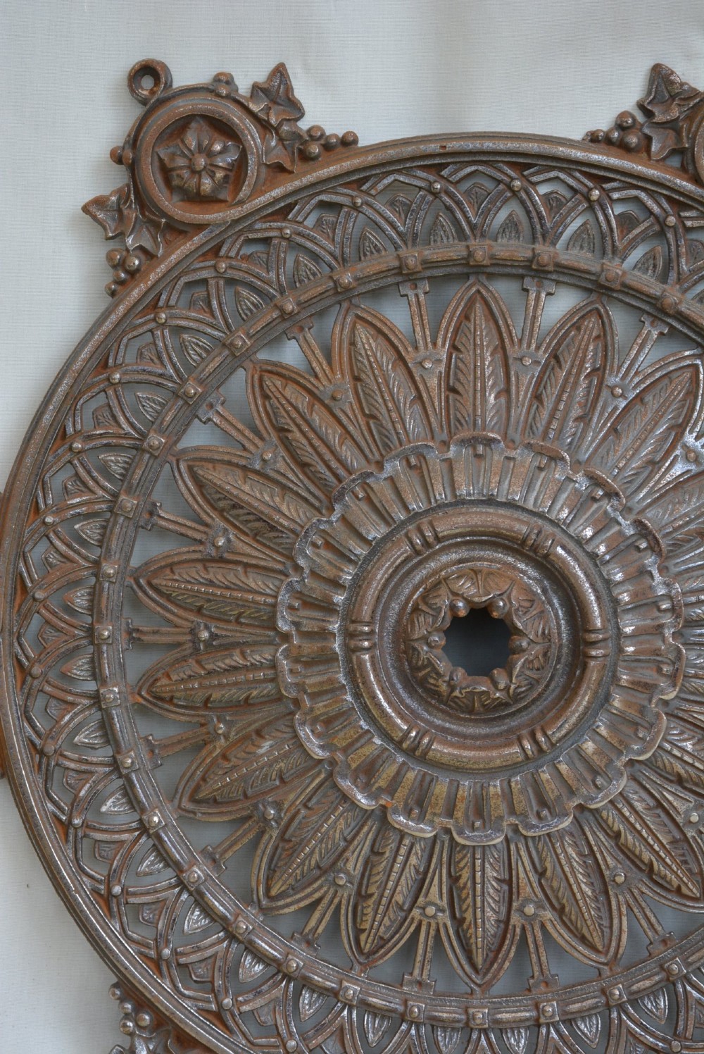 A circular Victorian cast iron ceiling rose featuring central feather relief detail surrounded by pierced openwork and ivy leaf border lugs. View VI