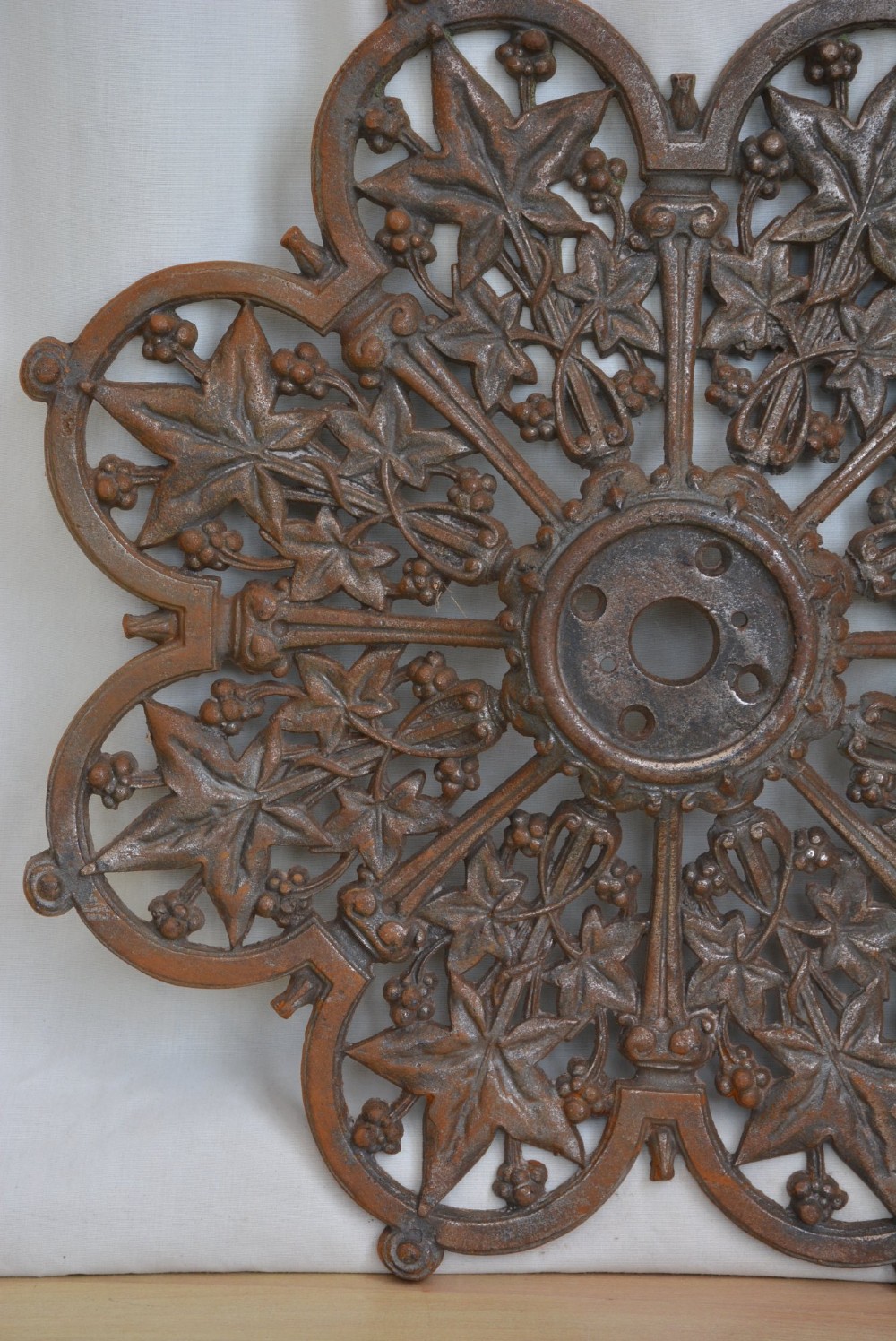 A circular Victorian cast iron ceiling rose featuring an openwork lobed design with raised ivy leaf and berry motifs surrounding a central circular aperture. View III