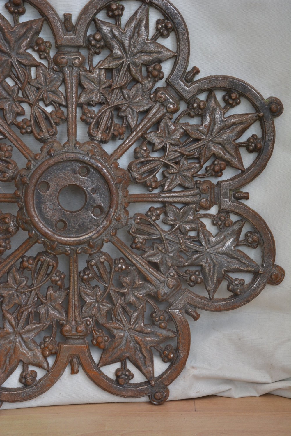 A circular Victorian cast iron ceiling rose featuring an openwork lobed design with raised ivy leaf and berry motifs surrounding a central circular aperture. View V
