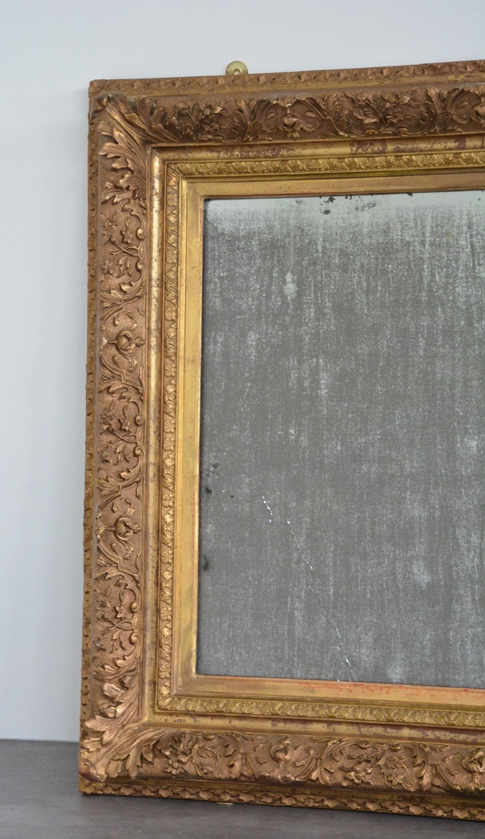 A rectangular antique wall mirror featuring a heavily carved gold giltwood frame and a foxed mirror glass plate. View II