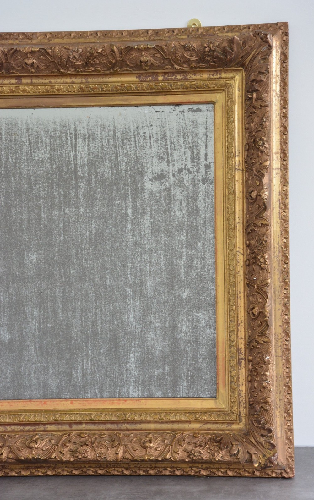A rectangular antique wall mirror featuring a heavily carved gold giltwood frame and a foxed mirror glass plate. View IV