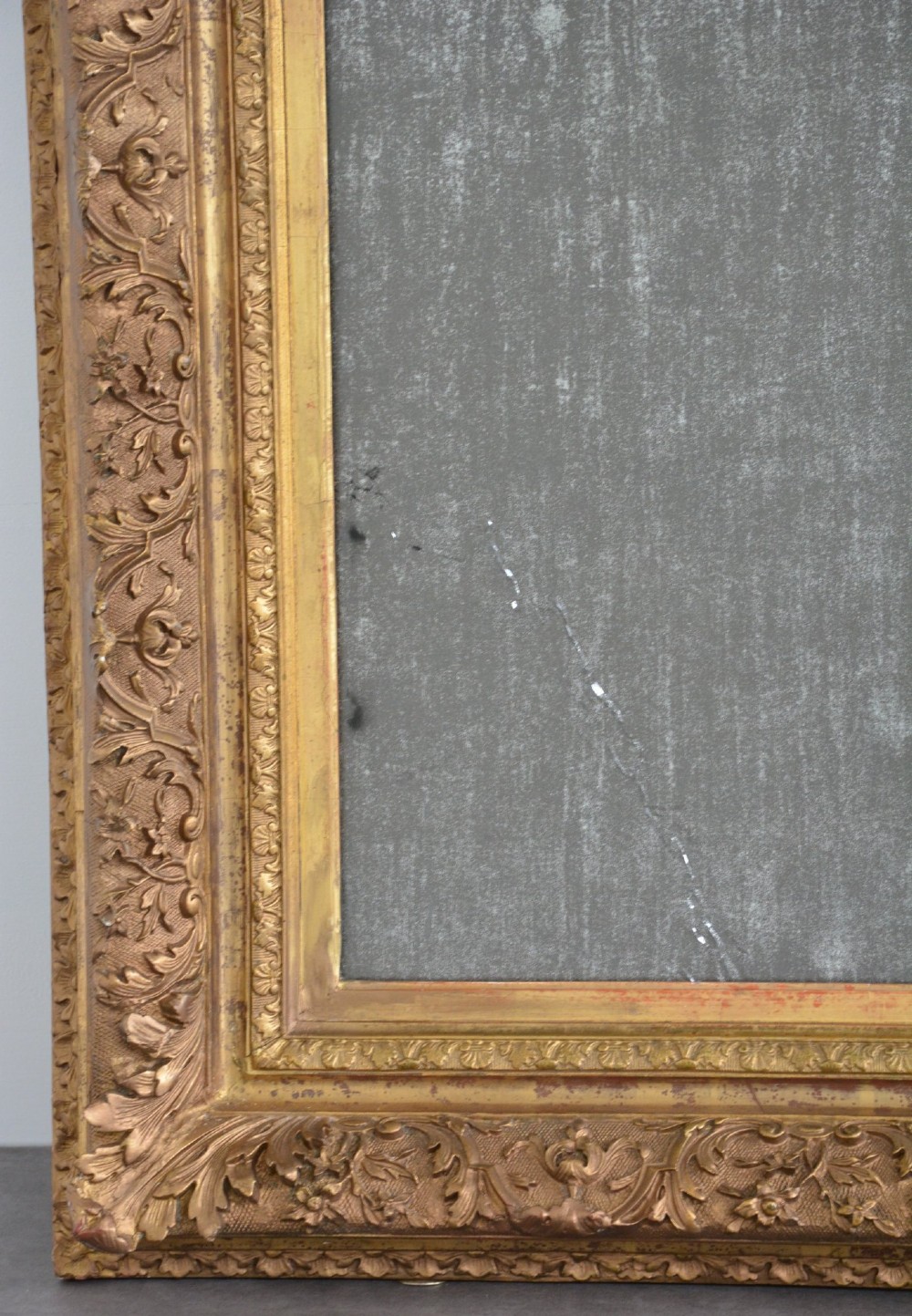 A rectangular antique wall mirror featuring a heavily carved gold giltwood frame and a foxed mirror glass plate. View V