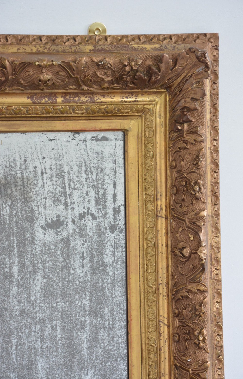 A rectangular antique wall mirror featuring a heavily carved gold giltwood frame and a foxed mirror glass plate. View VII