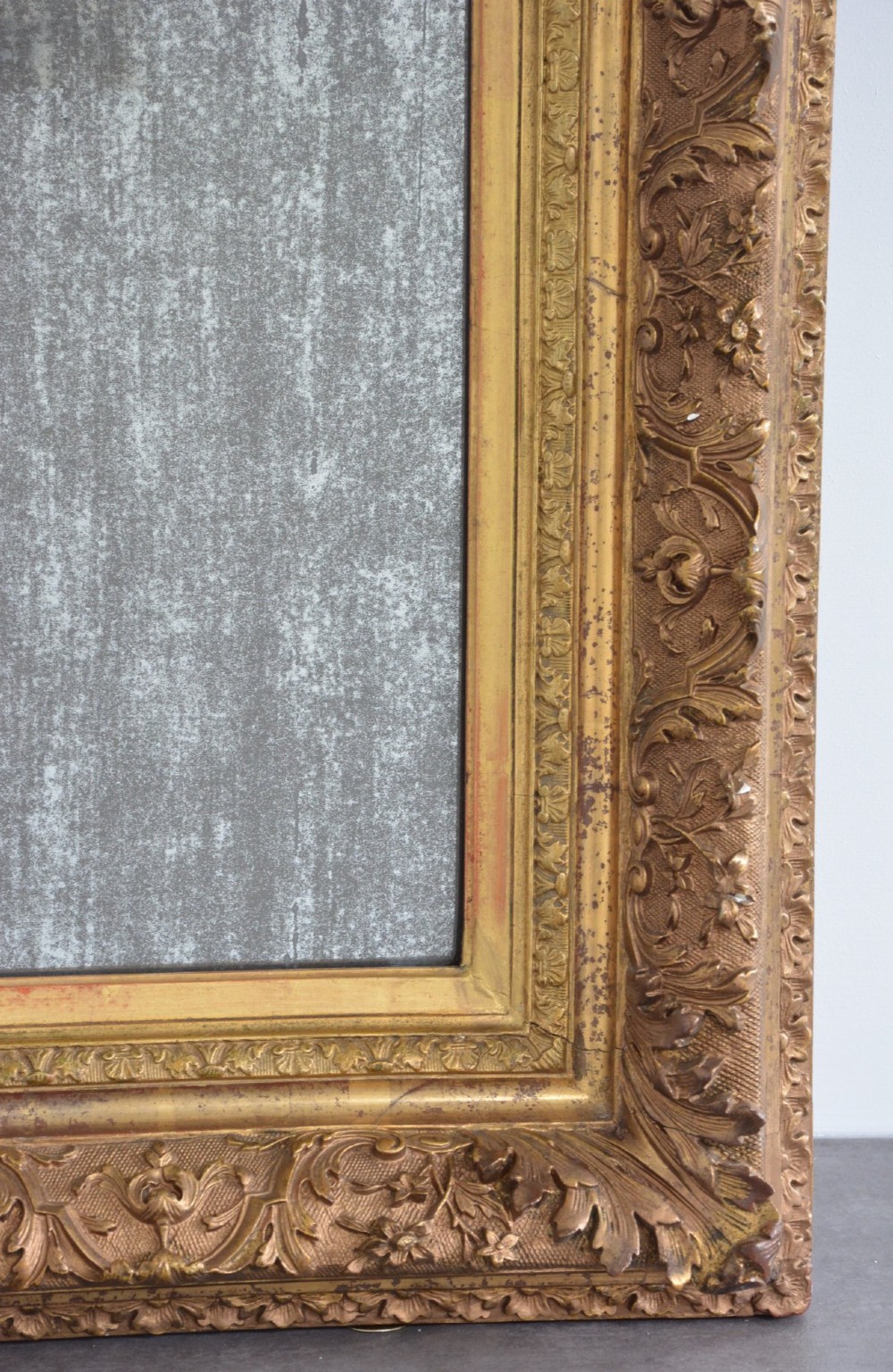 A rectangular antique wall mirror featuring a heavily carved gold giltwood frame and a foxed mirror glass plate. View VIII