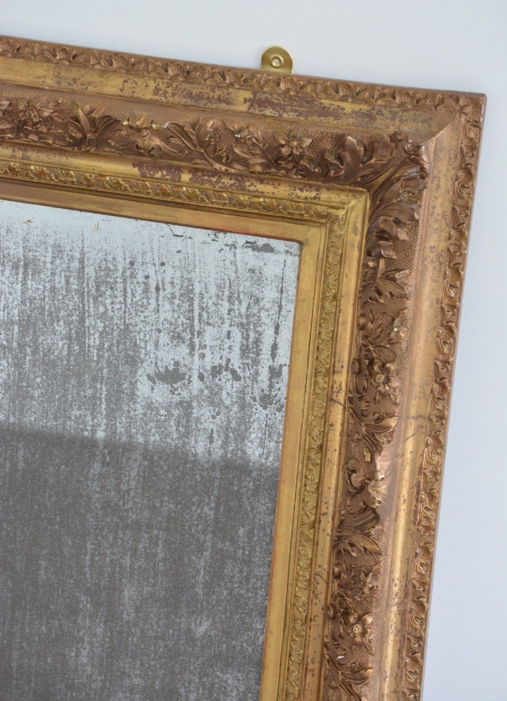 A rectangular antique wall mirror featuring a heavily carved gold giltwood frame and a foxed mirror glass plate. View X