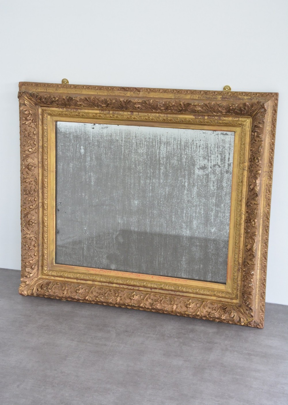 A rectangular antique wall mirror featuring a heavily carved gold giltwood frame and a foxed mirror glass plate. View XI