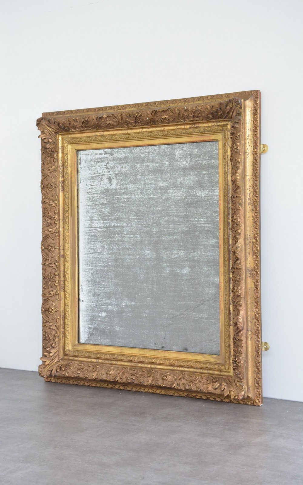 A rectangular antique wall mirror featuring a heavily carved gold giltwood frame and a foxed mirror glass plate.