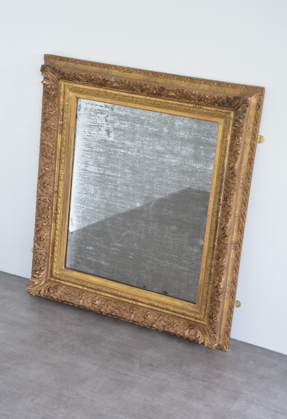 A rectangular antique wall mirror featuring a heavily carved gold giltwood frame and a foxed mirror glass plate. View XII