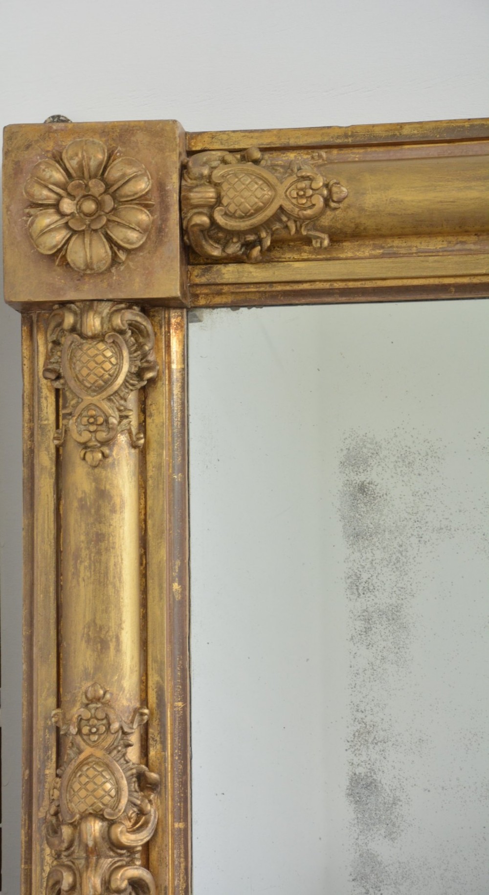 A large horizontal Regency style mirror featuring a gilded frame decorated with corner rosettes and floral mouldings enclosing foxed mirror glass. View II