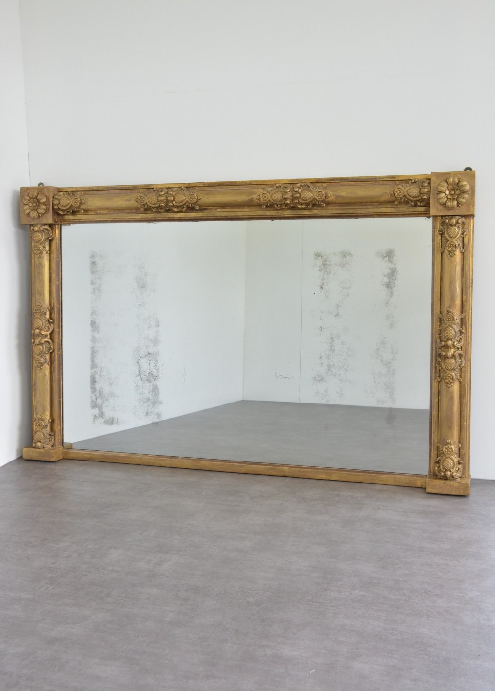 A large horizontal Regency style mirror featuring a gilded frame decorated with corner rosettes and floral mouldings enclosing foxed mirror glass.