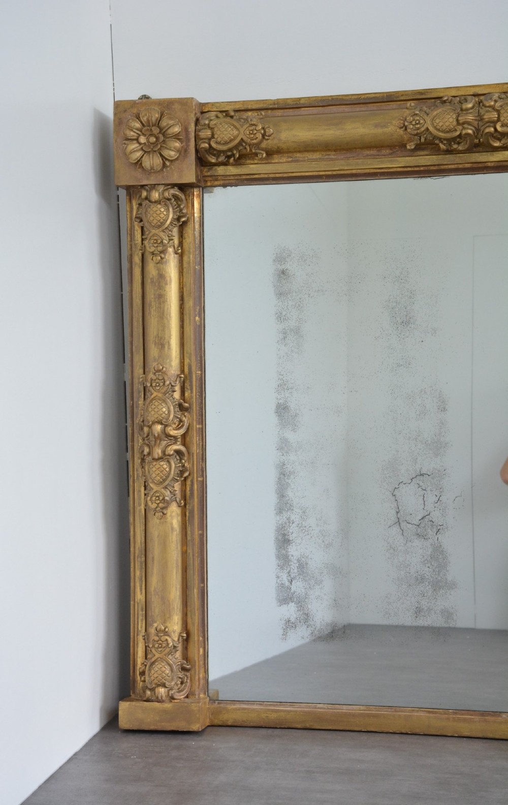 A large horizontal Regency style mirror featuring a gilded frame decorated with corner rosettes and floral mouldings enclosing foxed mirror glass. View V
